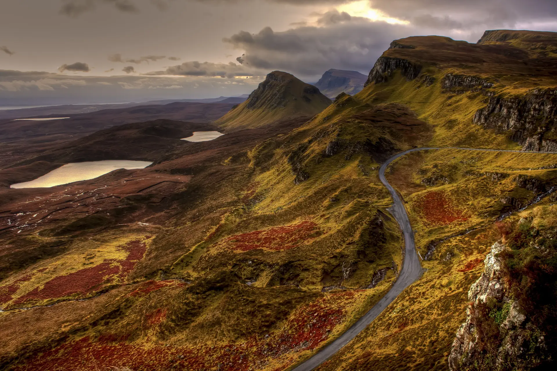 Panoramic Scottish mountains with winding roads beneath an atmospheric sky