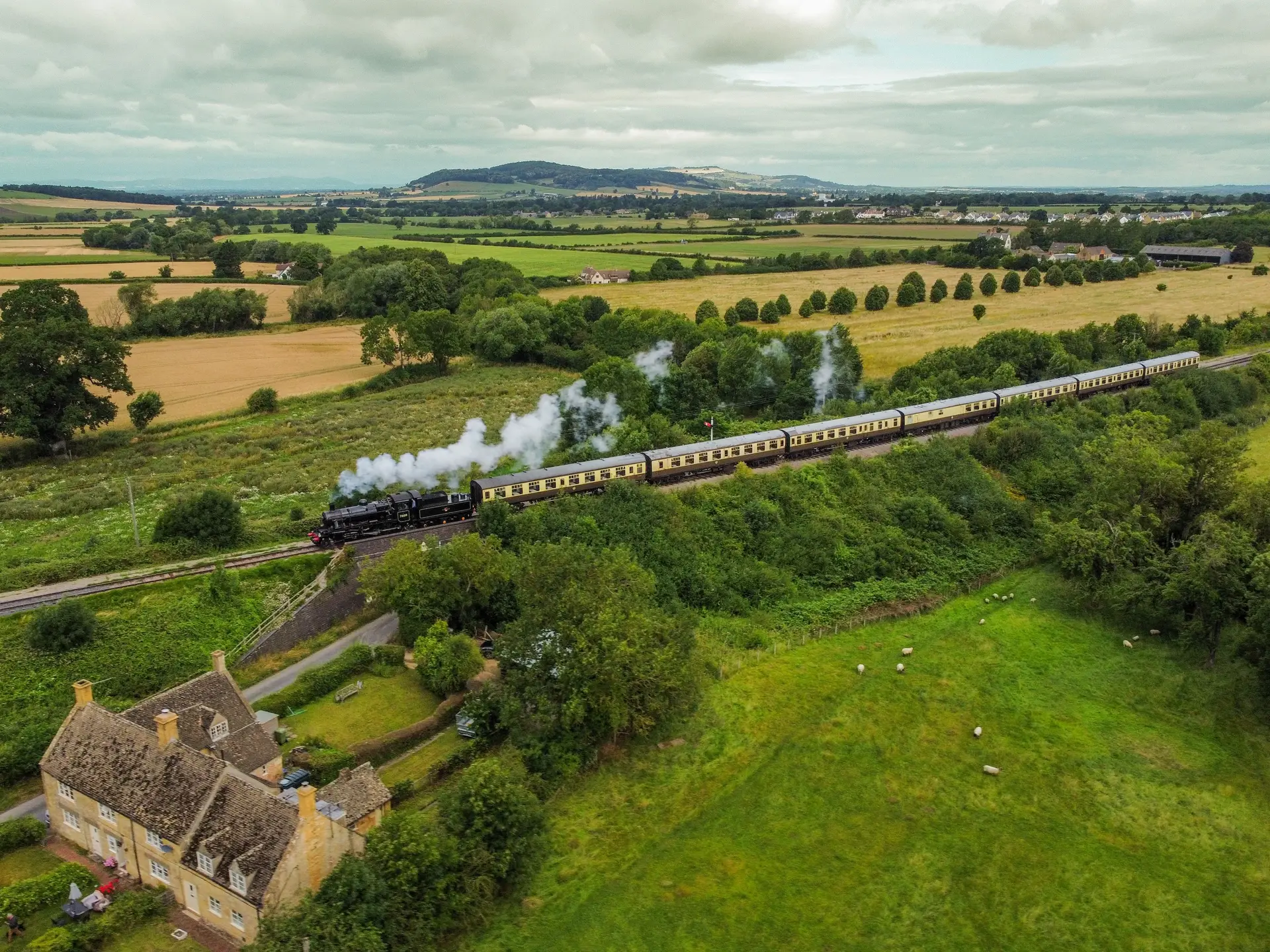 Scenic railway steam train crossing pastoral Cotswold hills in England