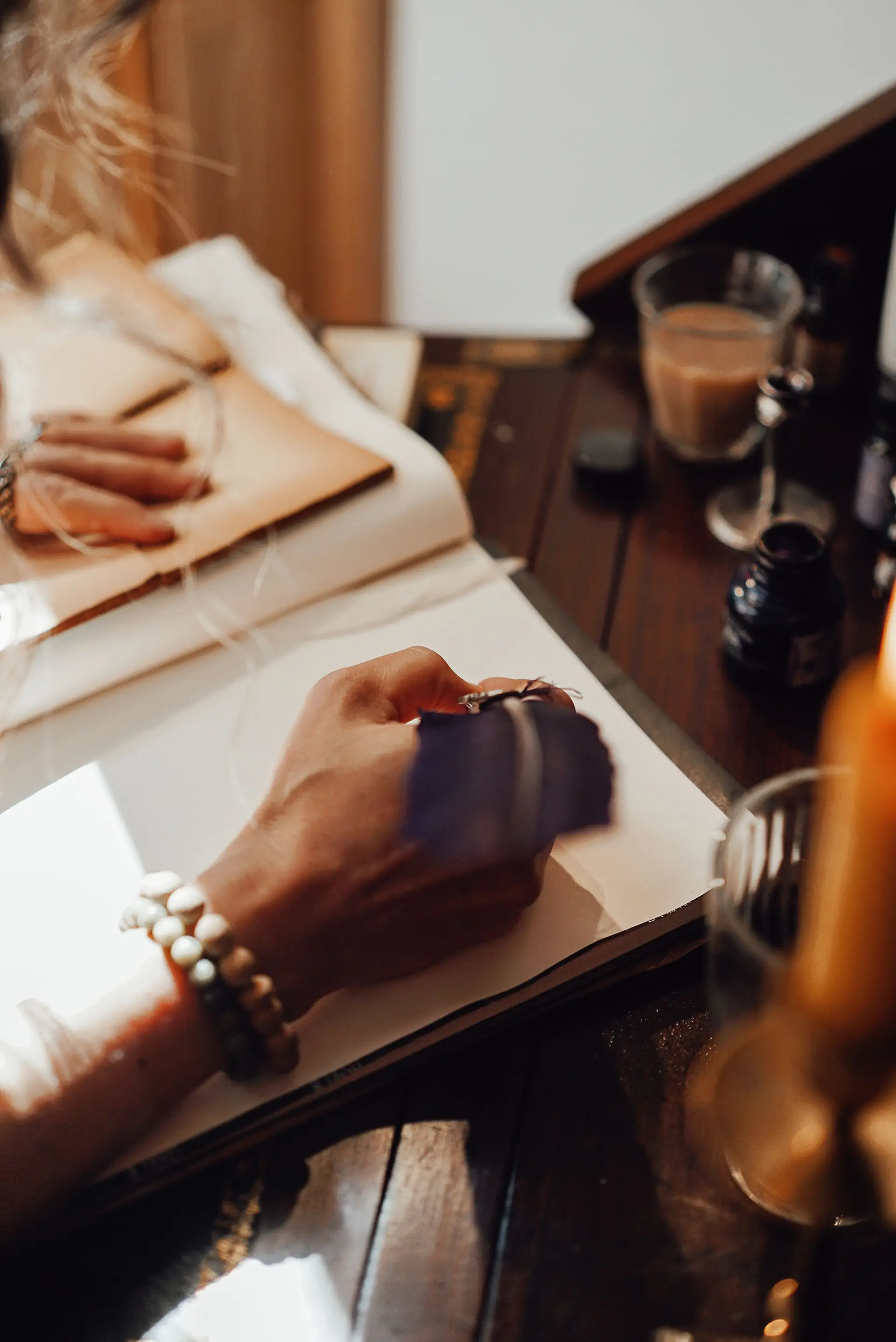 Writer taking notes in copybook with feather at vintage wooden table in natural light
